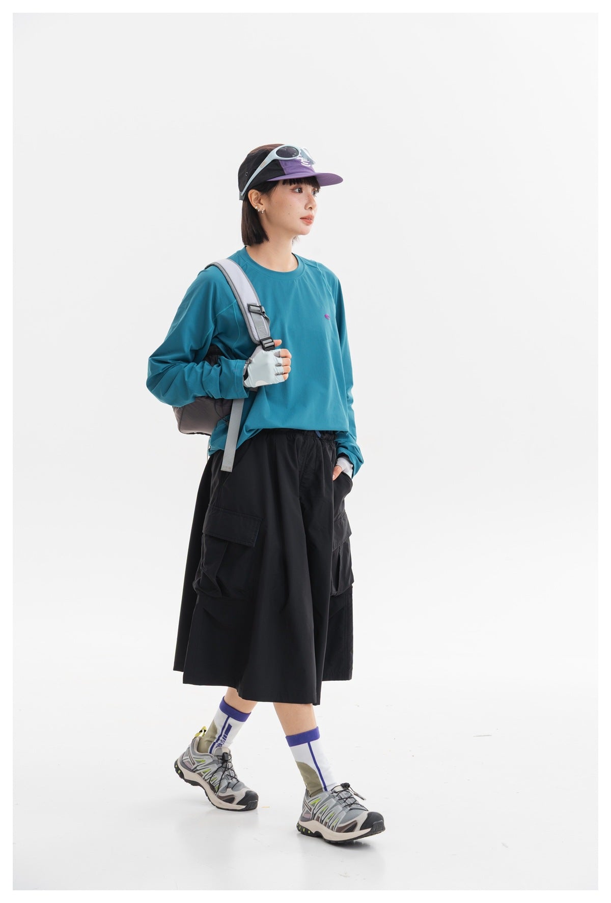 Model wearing a black knee-length cargo skirt with a teal long-sleeve top and outdoor accessories.