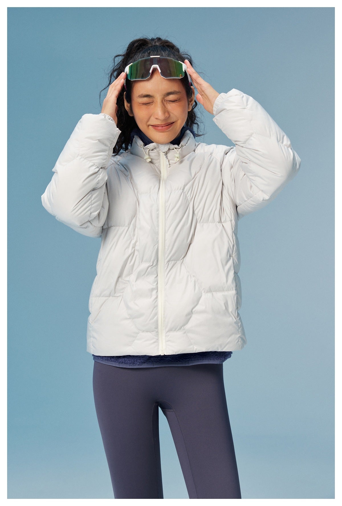 Front view of a woman wearing a white quilted puffer jacket, adjusting her sports sunglasses.