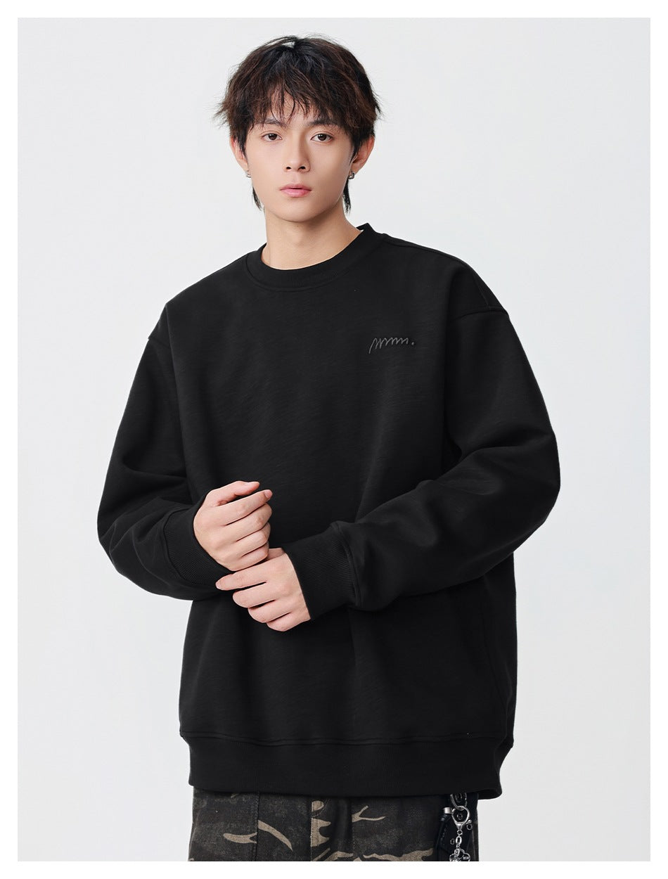 Model wearing a black crewneck sweatshirt with ribbed cuffs and hem and small tonal chest embroidery.
