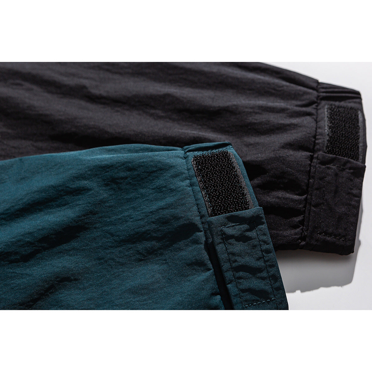 Close-up of black and deep teal jacket sleeves showing adjustable hook-and-loop cuffs.