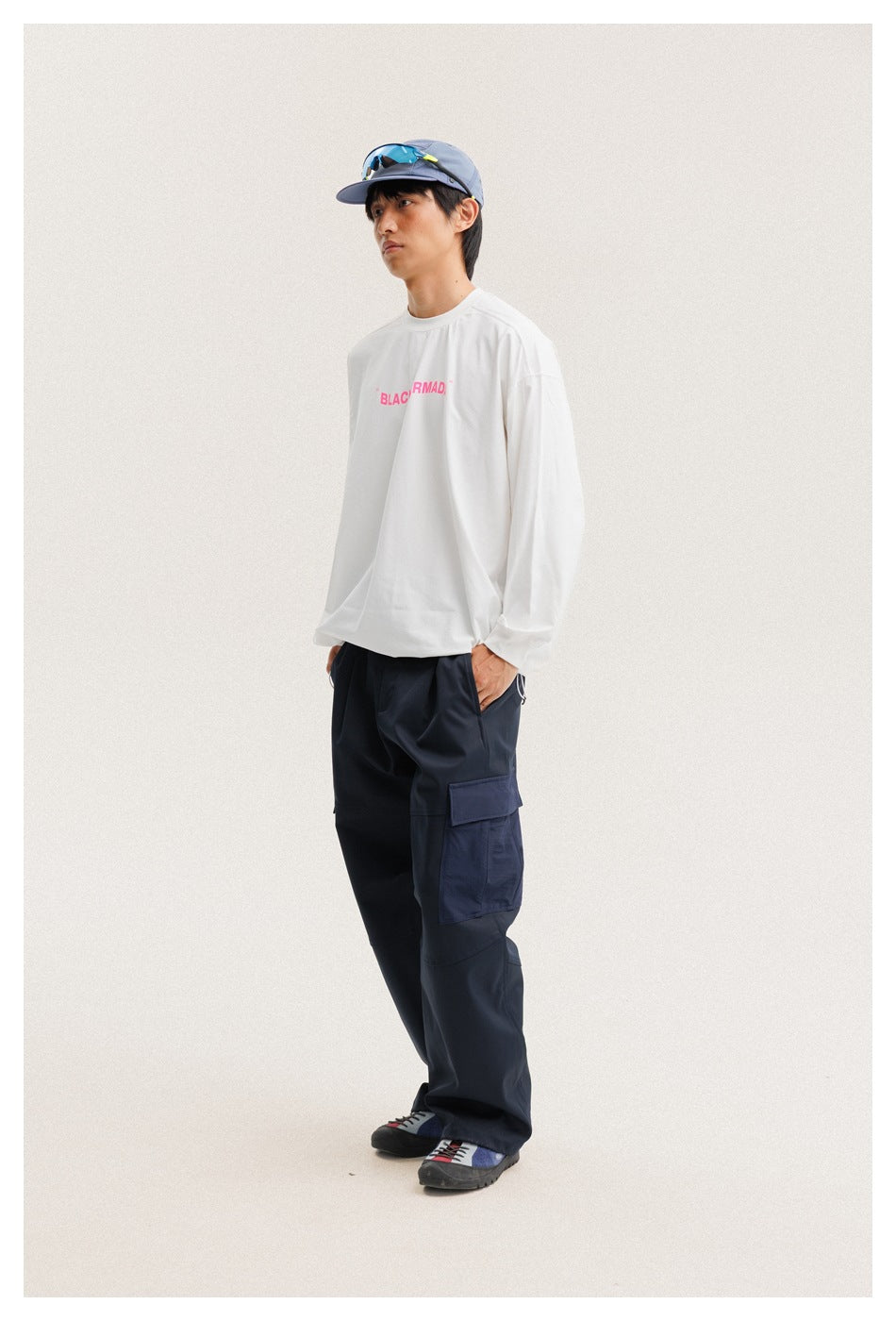 Side view of a model wearing a white long-sleeve shirt with pink text and navy cargo pants.