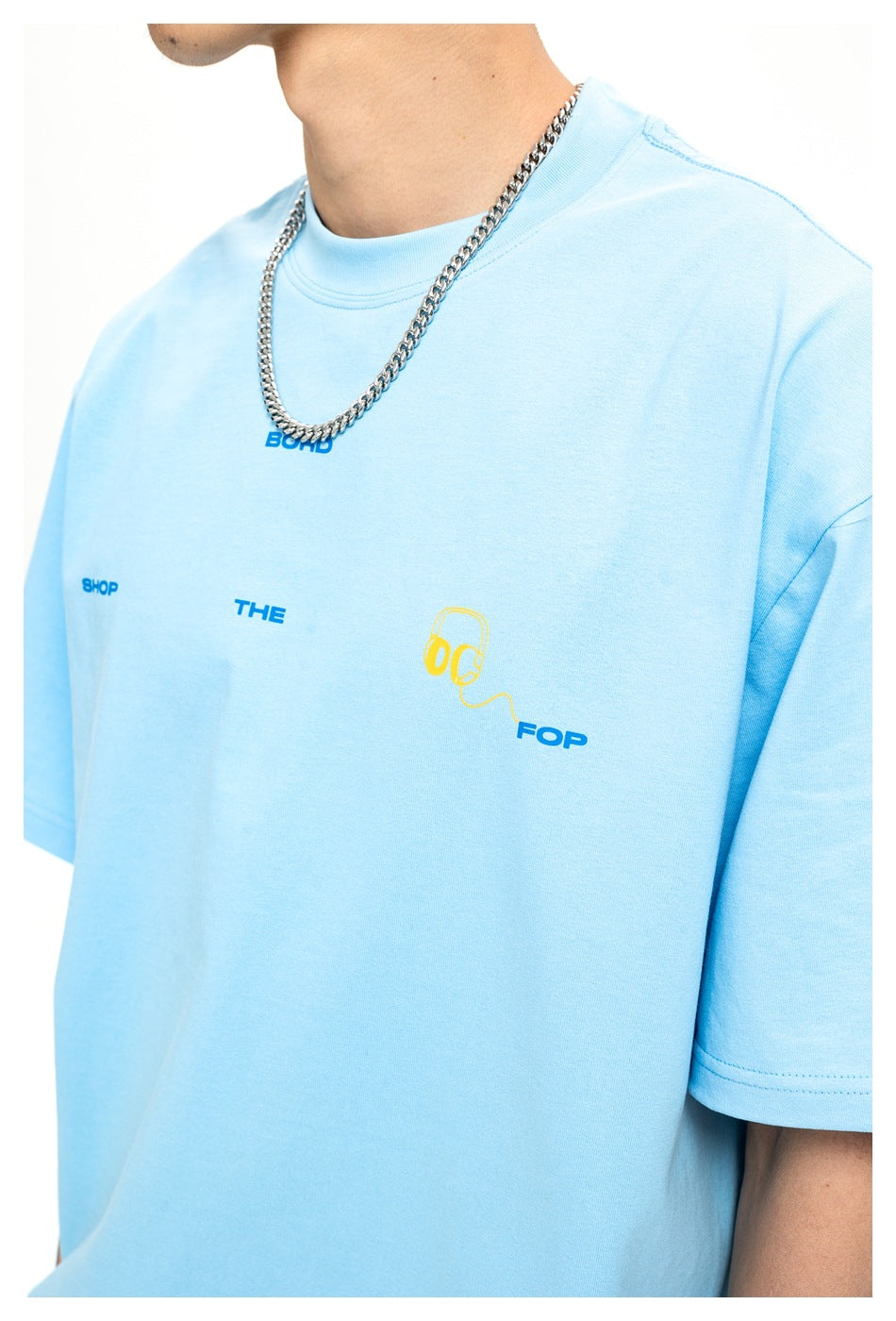 Close-up of a light blue T-shirt with small blue lettering and a yellow headphone graphic on the chest.