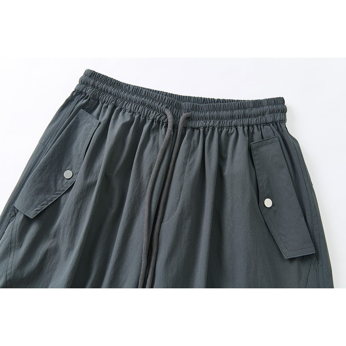 Close-up of dark charcoal cargo pants with an elastic drawstring waist and snap-button flap pockets.