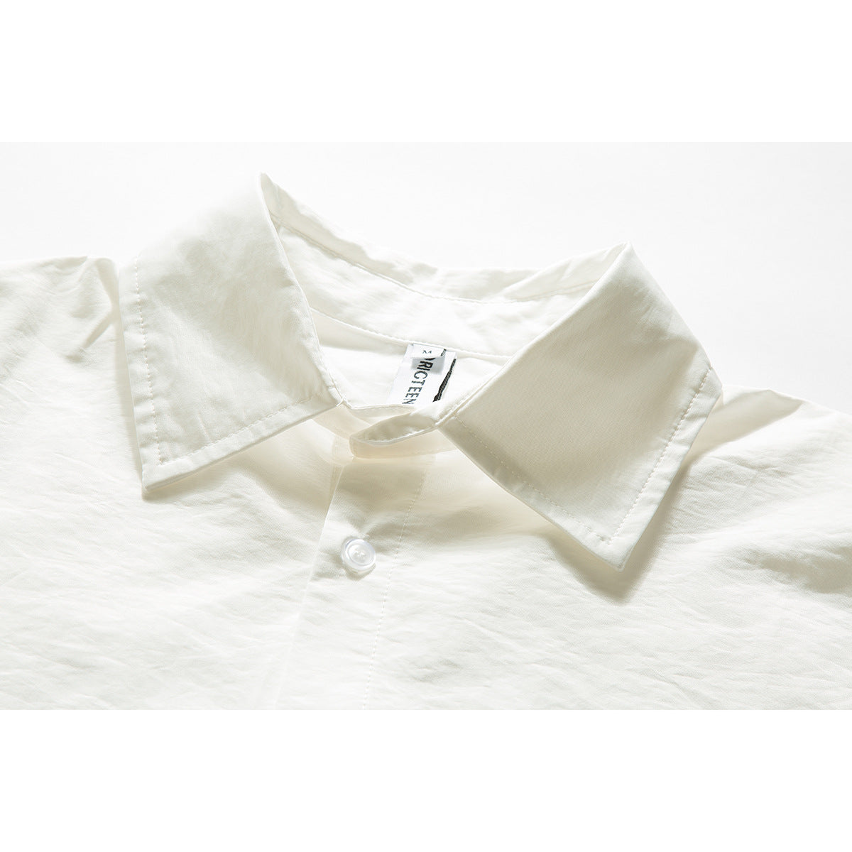 Close-up of an ivory shirt collar, neckline label, and a white button.