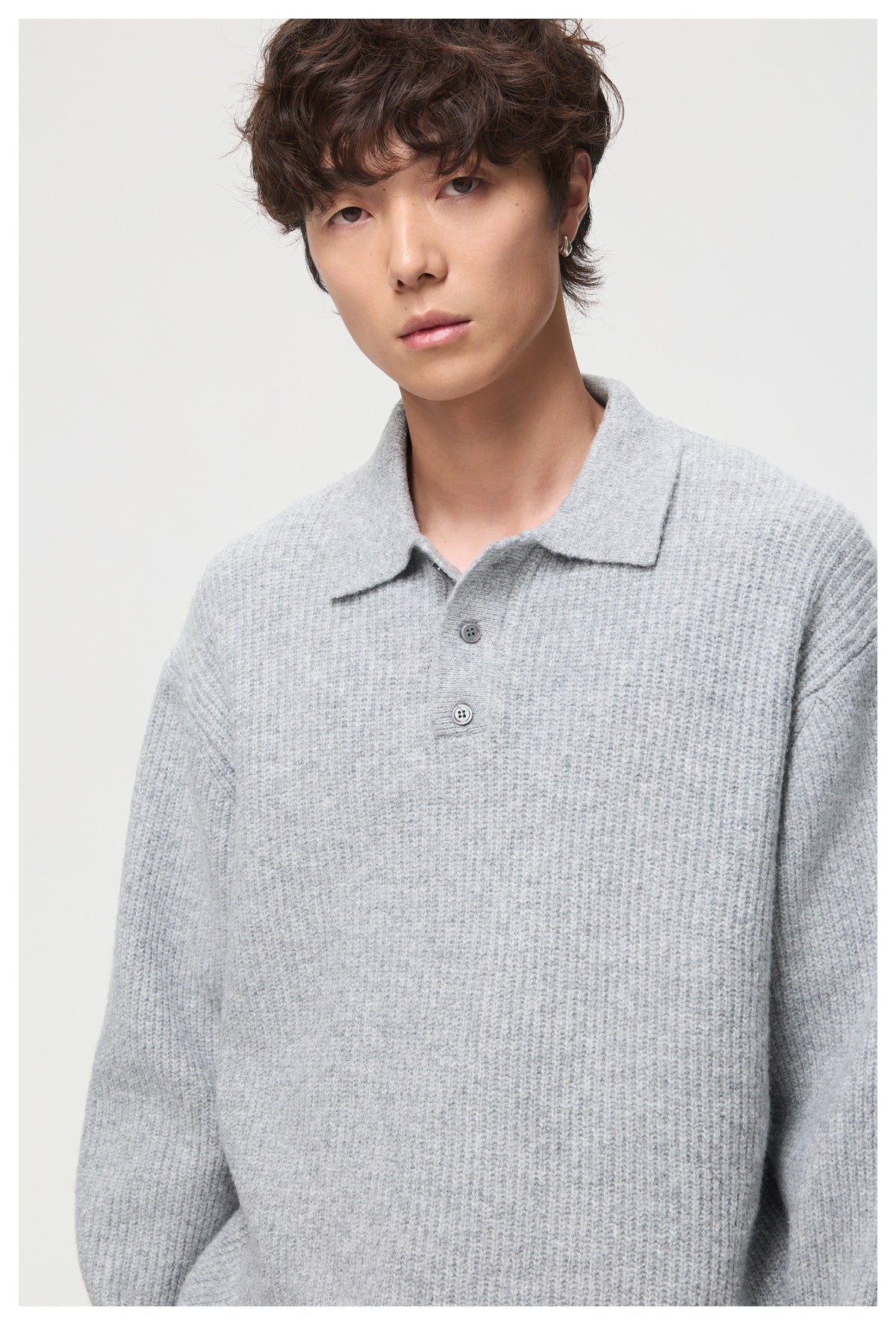 Close front view of a model wearing a light gray textured knit polo sweater with a collar and two visible buttons.