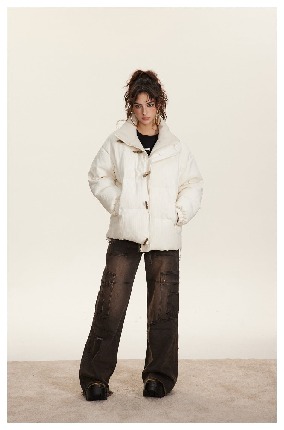 Full-length model wearing an ivory padded jacket with a high collar and wooden toggles, styled with dark cargo pants.