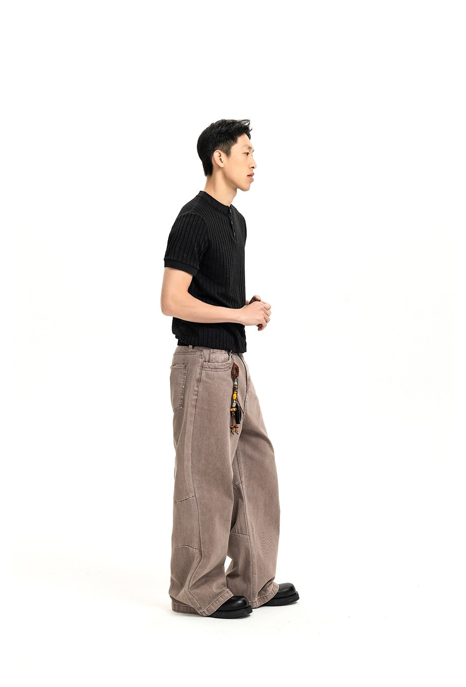 Side view of a model wearing a black ribbed short-sleeve henley and loose taupe jeans.