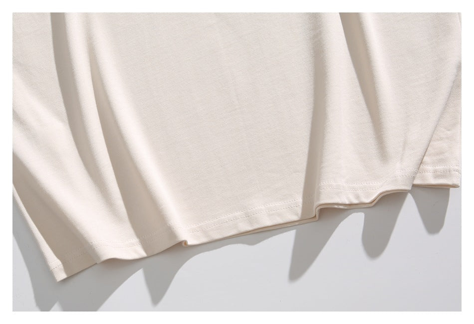 Close-up of the stitched lower hem and drape of an ivory T-shirt.