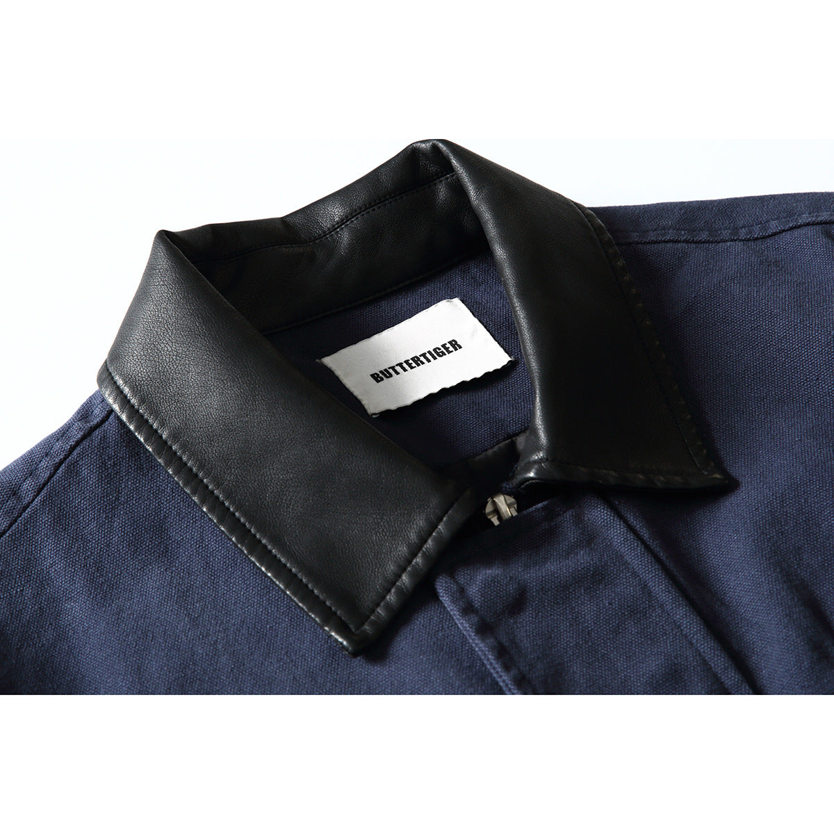 Close-up of a navy jacket with a black textured collar, front zipper, and a visible BUTTERTIGER neck label.