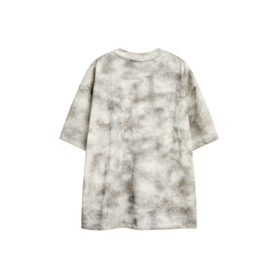 Flat lay of an oversized beige-gray tie-dye short-sleeve crew-neck T-shirt with scattered white and blue splatter marks.