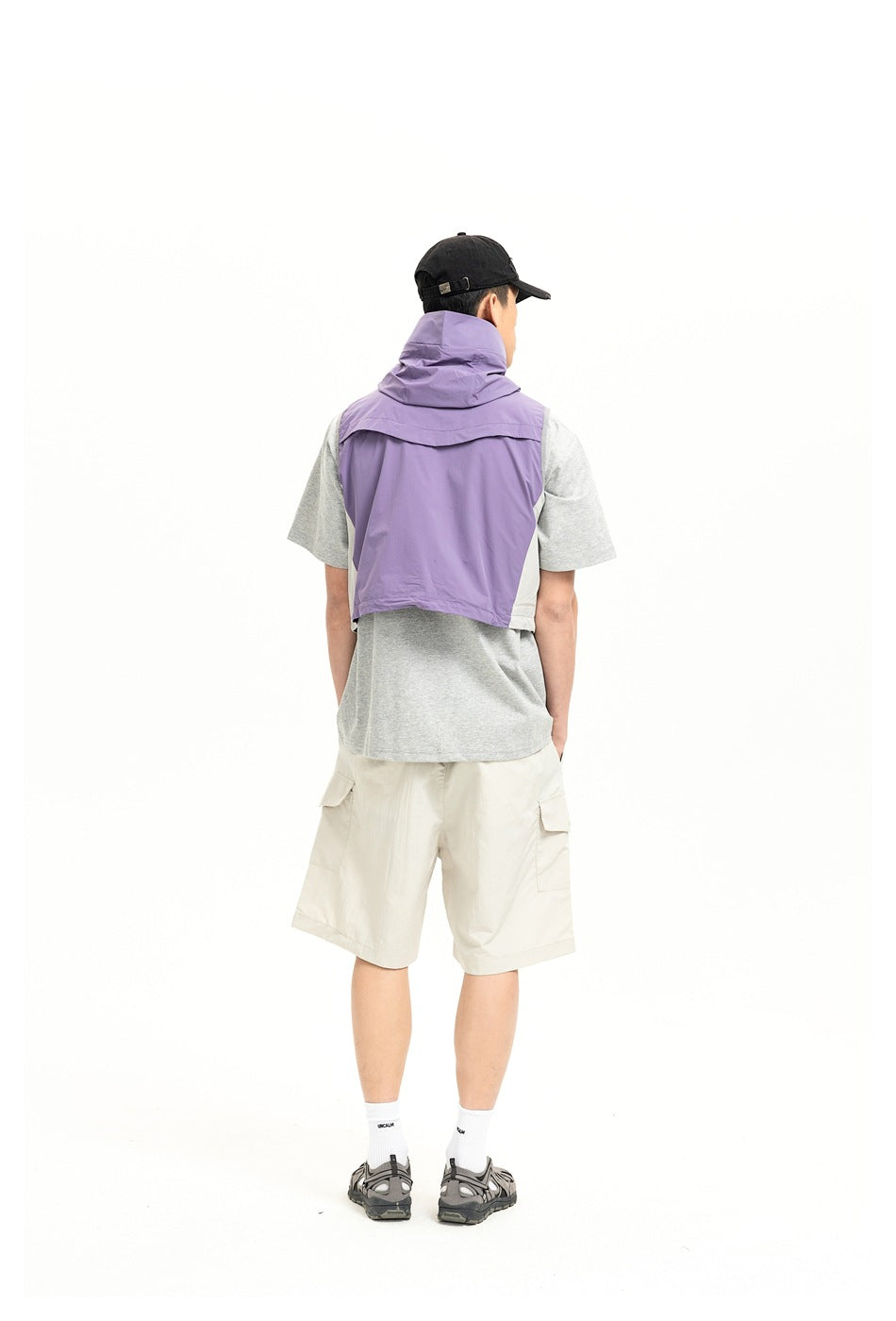 Back view of a model wearing a purple hooded vest over a gray T-shirt with cream cargo shorts.