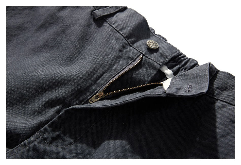 Close-up of charcoal trousers showing the waistband button and partially open zipper fly.