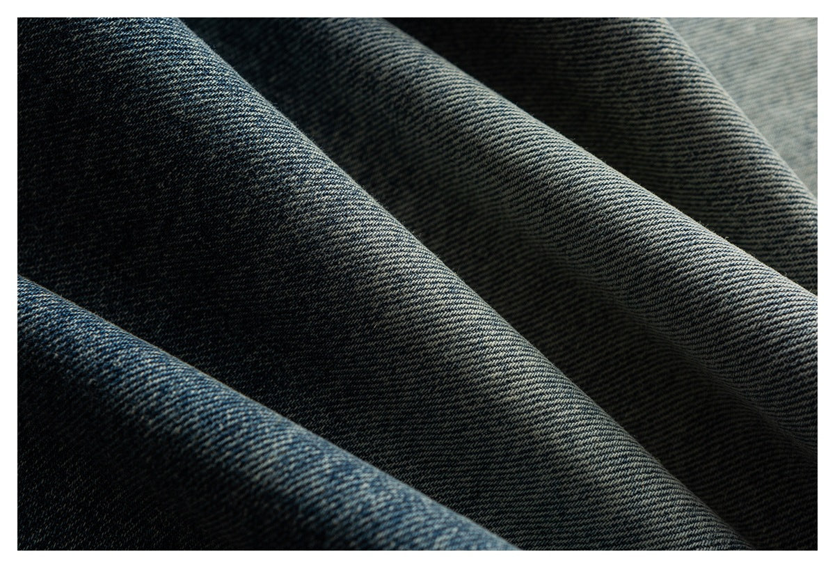Close-up of dark blue denim draped in folds, showing its diagonal weave and subtle fading.
