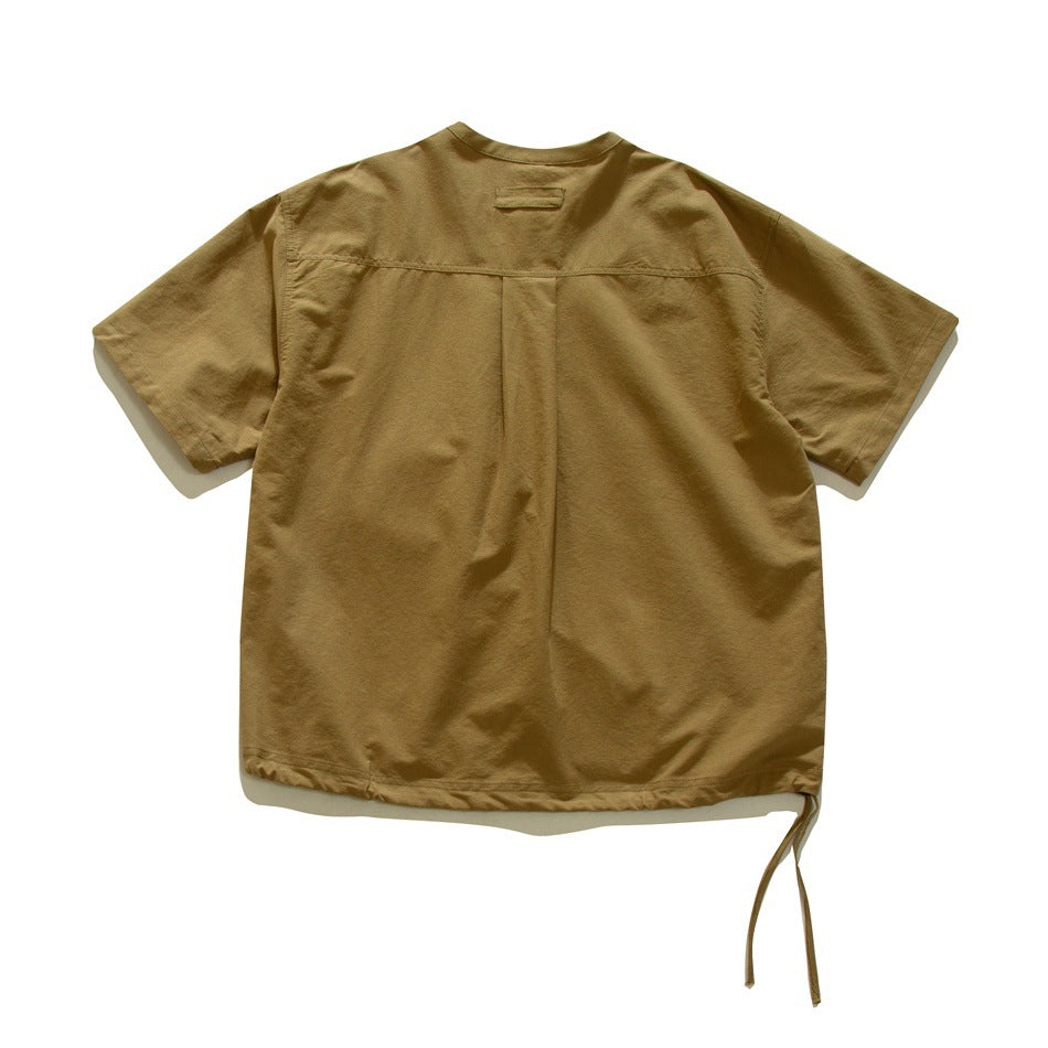 Back view of a tan short-sleeve shirt with a shoulder yoke, center pleat, and adjustable hem ties.