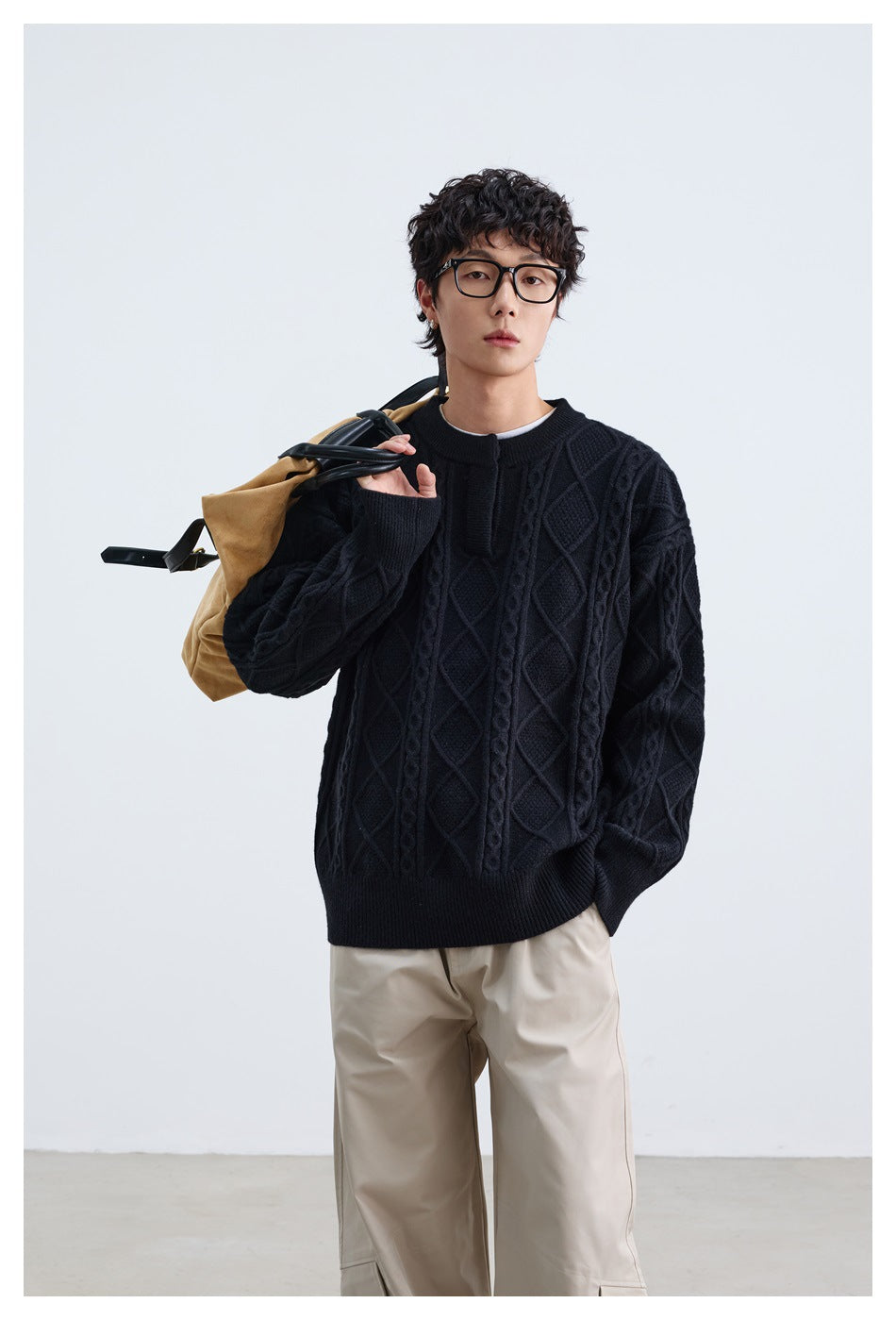 Model wearing a black cable-knit sweater with raised diamond patterns and ribbed trim, carrying a tan bag.