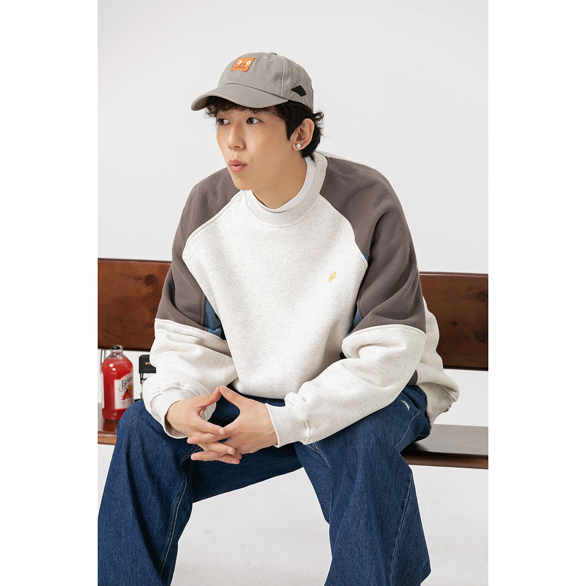 Seated model wearing an off-white color-block raglan sweatshirt with gray shoulders and blue side panels.