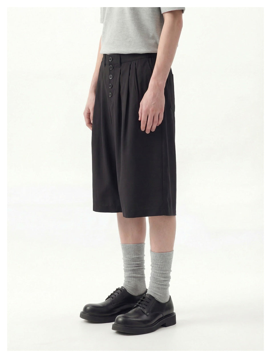 Front view of a model wearing black knee-length wide-leg shorts with a five-button waistband and pleats.