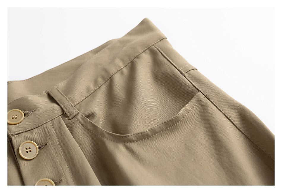 Close-up of tan trousers showing the waistband, belt loop, front button, and curved front pocket.