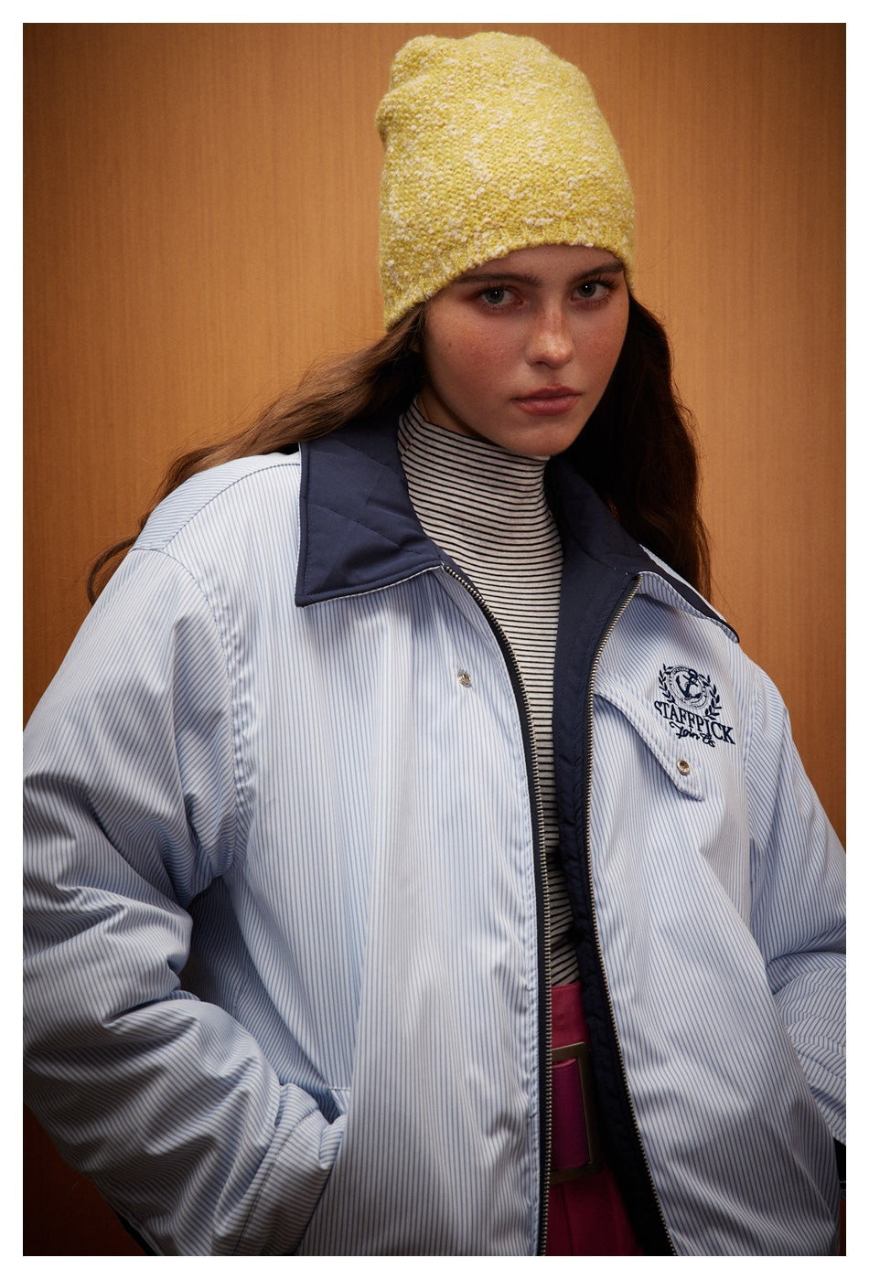 Close view of a model wearing a light blue pinstriped jacket with navy collar and embroidered chest emblem.