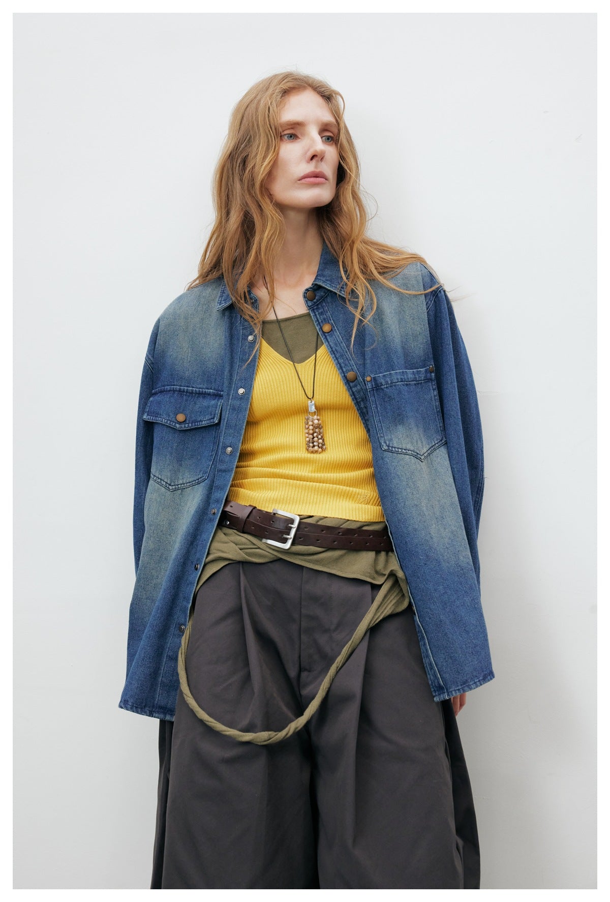Model wearing an oversized blue denim shirt jacket with two chest pockets and snap buttons.