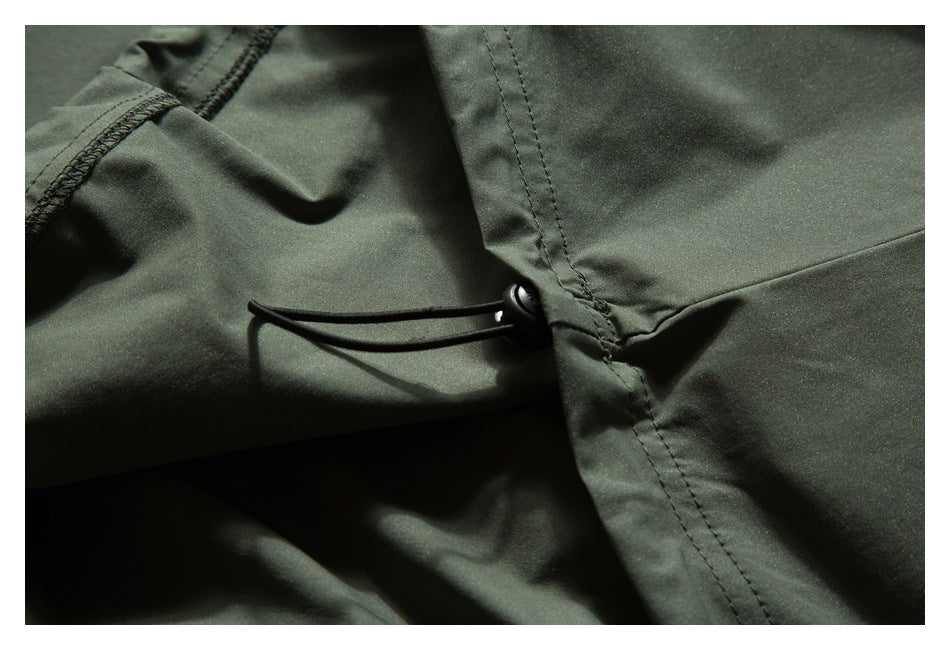 Close-up of a black drawcord adjuster at a seam on dark olive-green fabric.