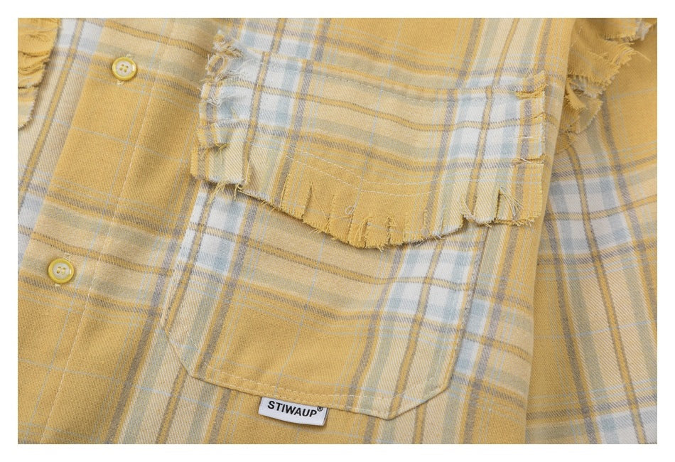 Close-up of a frayed chest pocket, yellow buttons, and plaid pattern on the shirt.