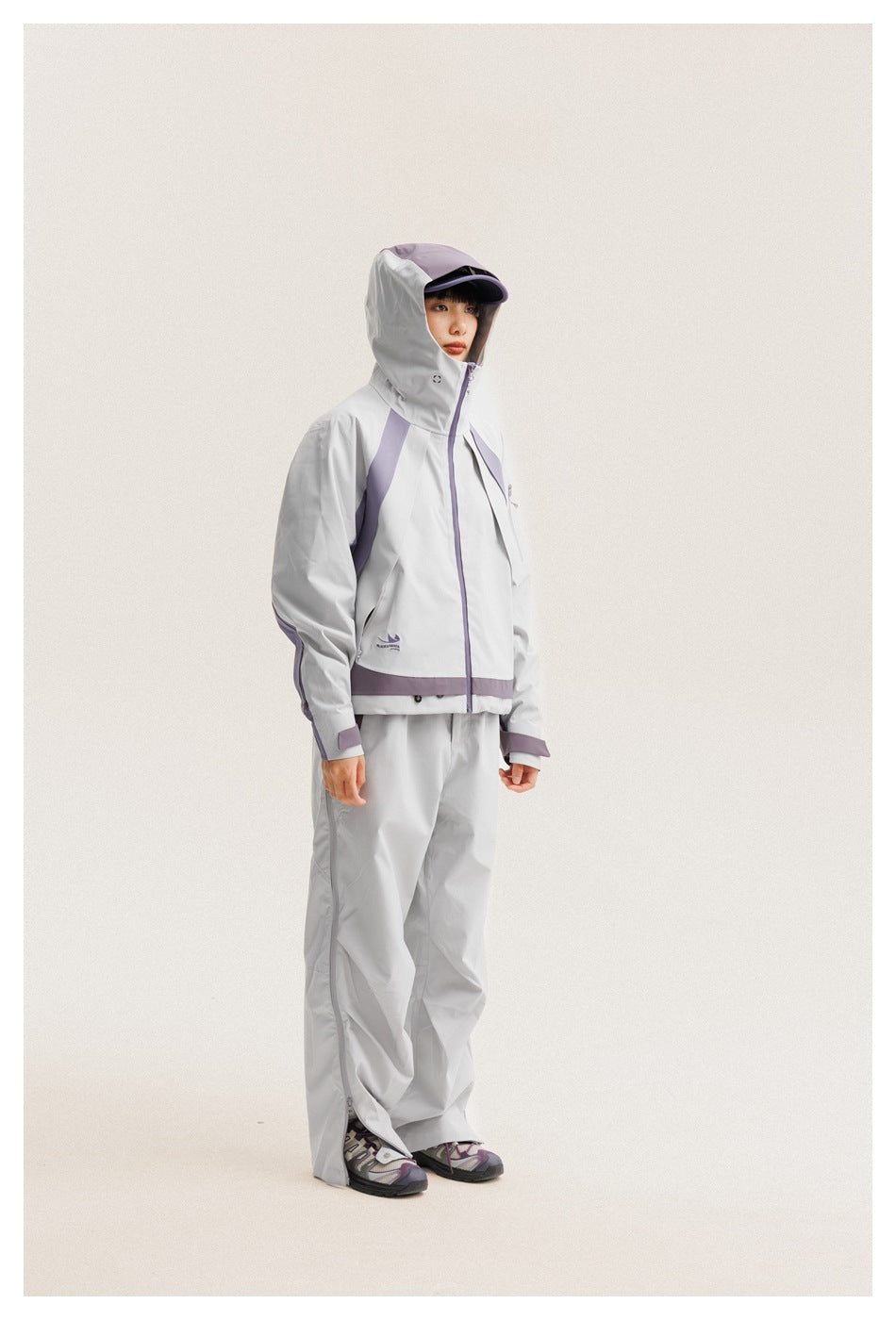 Model wearing a light gray hooded jacket with lavender trim and matching pants, shown full length from the front.