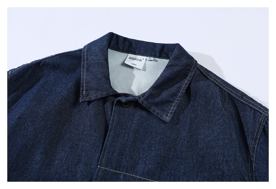 Upper portion of a dark indigo denim shirt showing its pointed collar, black button, and sewn-in neck label.