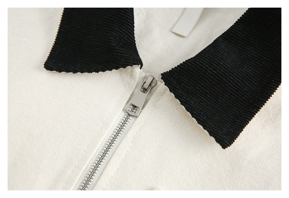 Close-up of a cream garment's metal zipper and wide black ribbed collar.