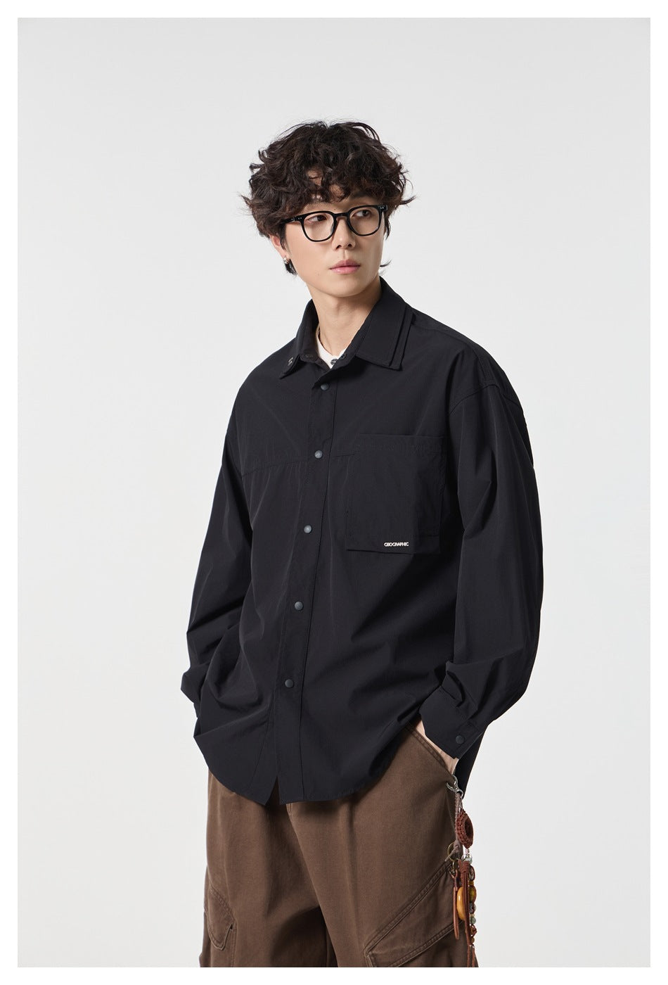 Model wearing a black oversized button-front shirt with a pointed collar and single chest pocket.