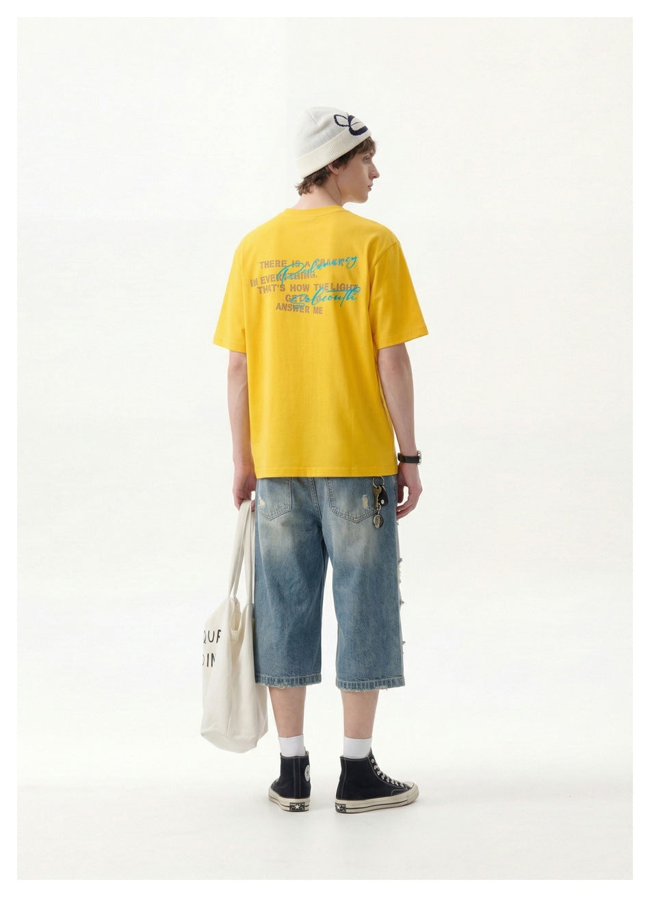 Back view of a model wearing a yellow graphic T-shirt and denim shorts.