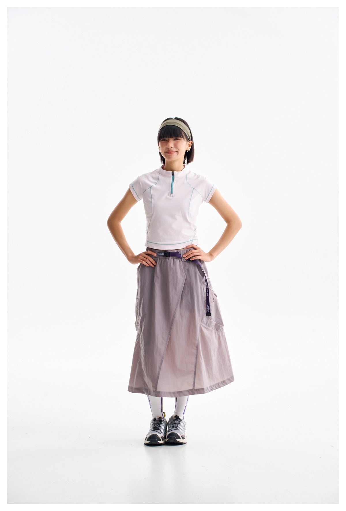 Full-length model wearing a pale pink zip-neck top and a gray-lilac wrap-style midi skirt.