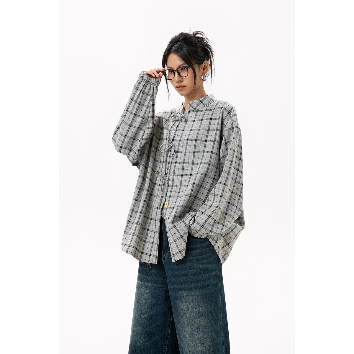 Model wearing a gray plaid blouse with loop closures and voluminous sleeves, paired with dark wide-leg jeans.
