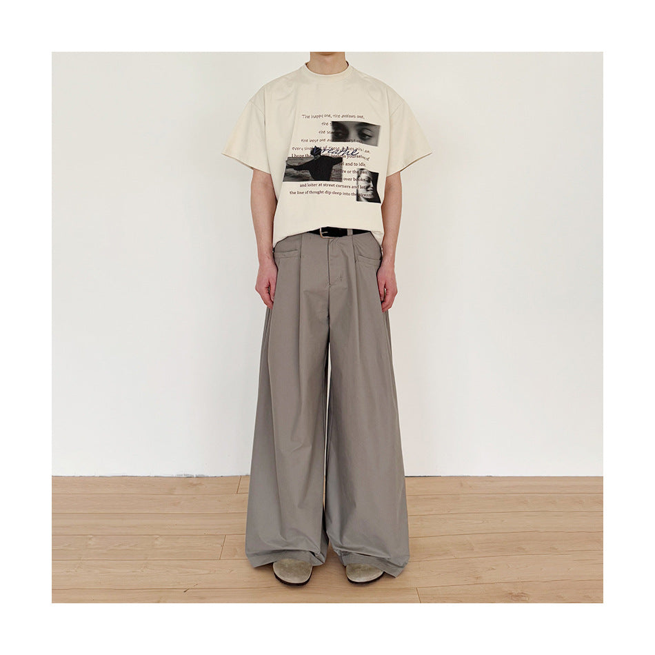 Model wearing gray wide-leg pleated trousers with a cream graphic tee and black belt, full-length front view
