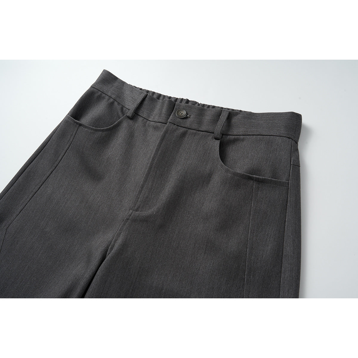 Close-up of charcoal gray trousers showing the waistband, button, belt loops, and curved front pockets.