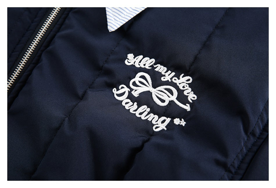 Close-up of white embroidered lettering and a bow motif on the navy jacket beside its zipper.