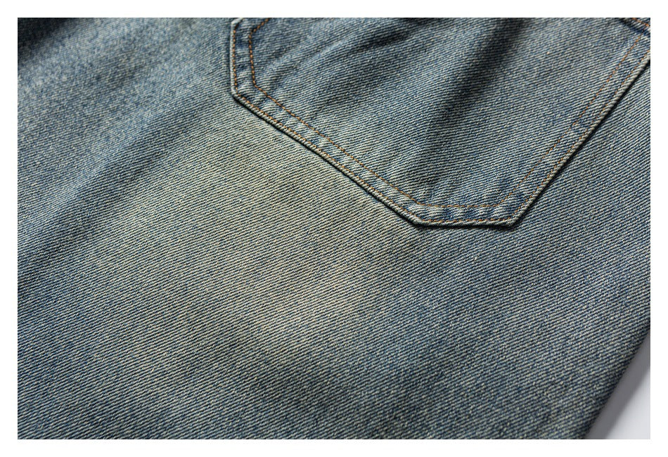 Close-up of blue denim showing a curved pocket edge with tan stitching.