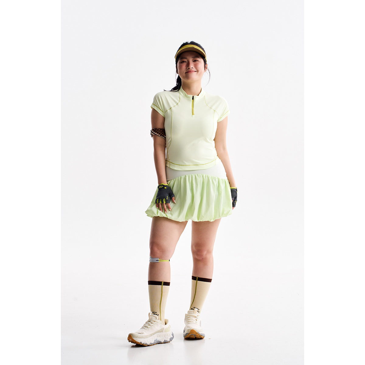 Model wearing a pale yellow zip-neck athletic top and matching skirt against a white studio background.