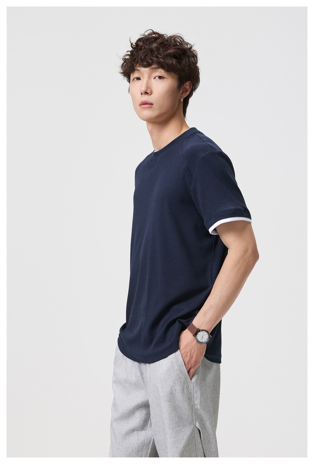 Three-quarter view of a model wearing a navy T-shirt with white sleeve-cuff trim.