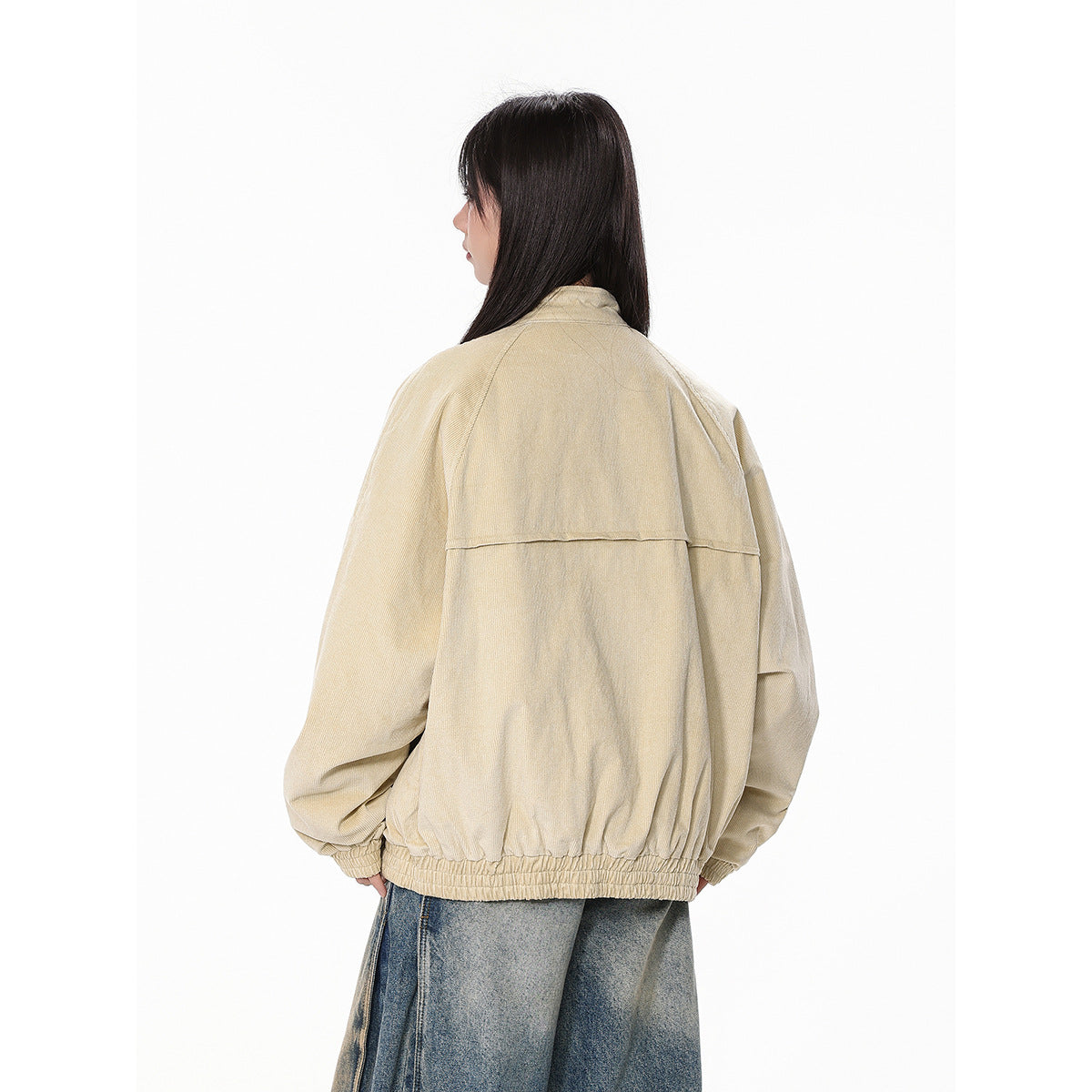Rear view of a model wearing a beige oversized jacket with a horizontal back yoke and gathered hem.