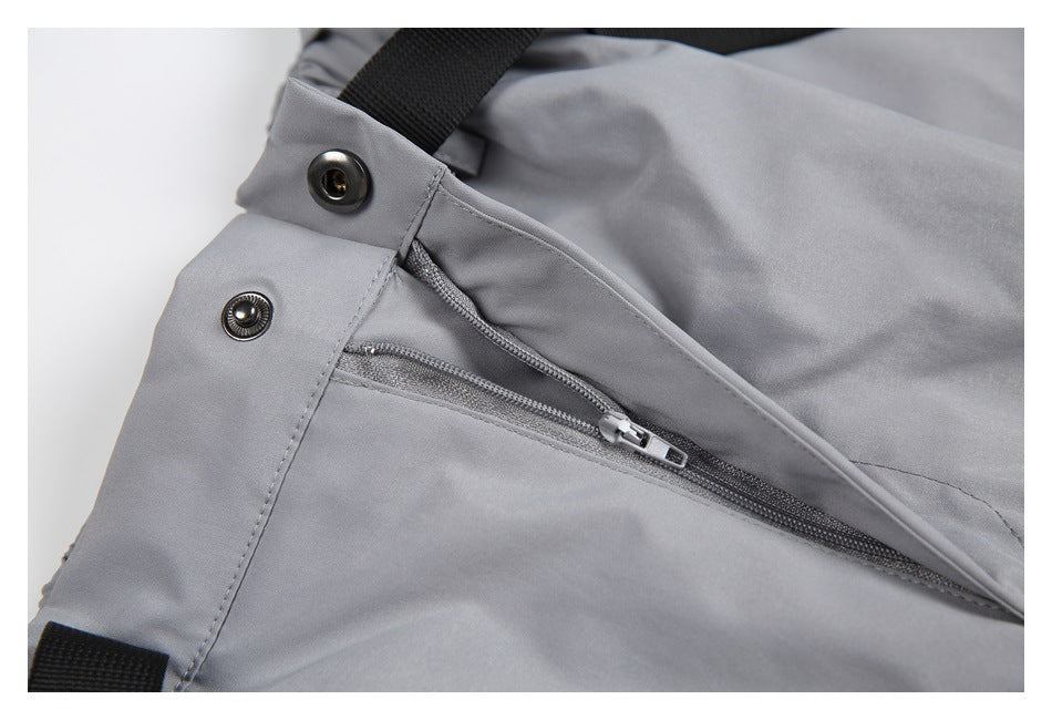 Close-up of gray pants with a zippered pocket, snap fasteners, and black webbing trim.