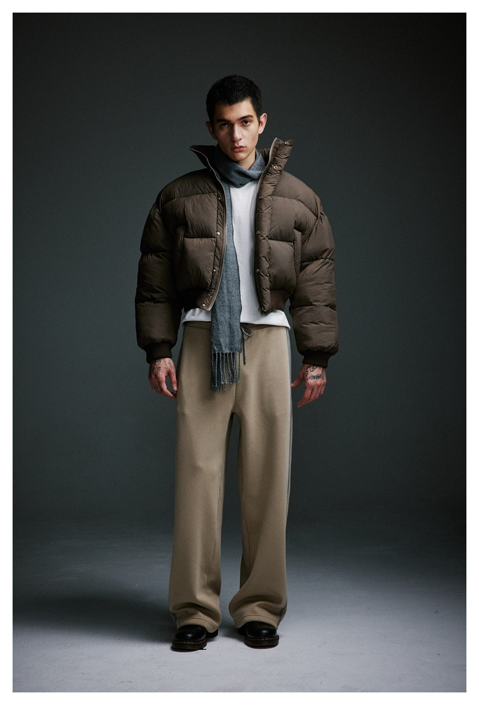 Full-length view of a person wearing khaki wide-leg side-stripe sweatpants with a puffer jacket and black boots