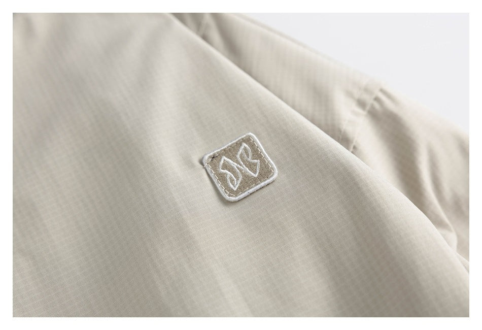 Close-up of a small embroidered emblem on the cream jacket fabric.