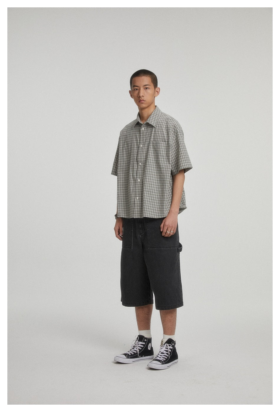 Three-quarter view of a model wearing a gray plaid short-sleeve button-up shirt with a chest pocket.