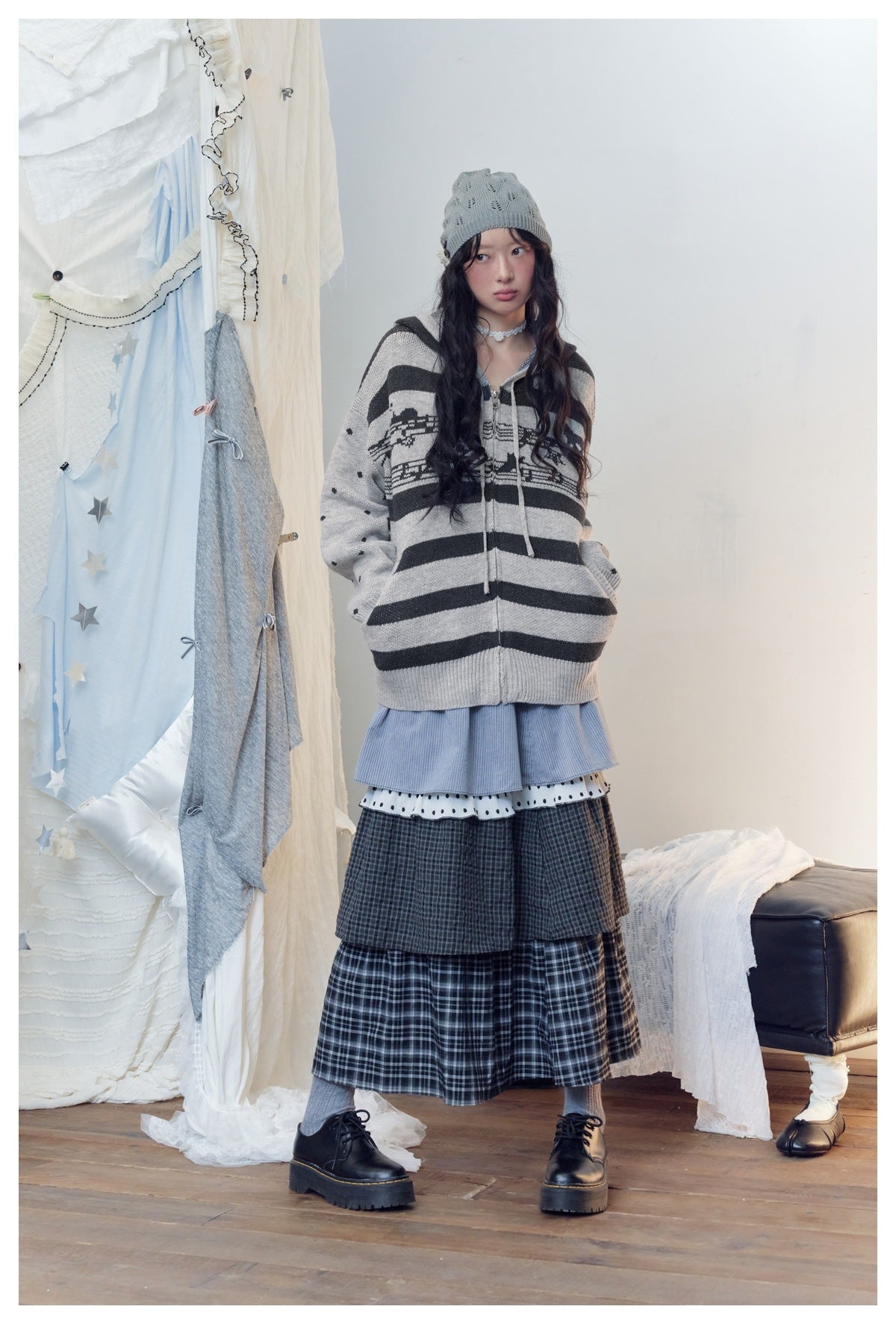 Full-length model wearing a gray-and-black striped hooded sweater with dotted sleeves and a layered skirt.
