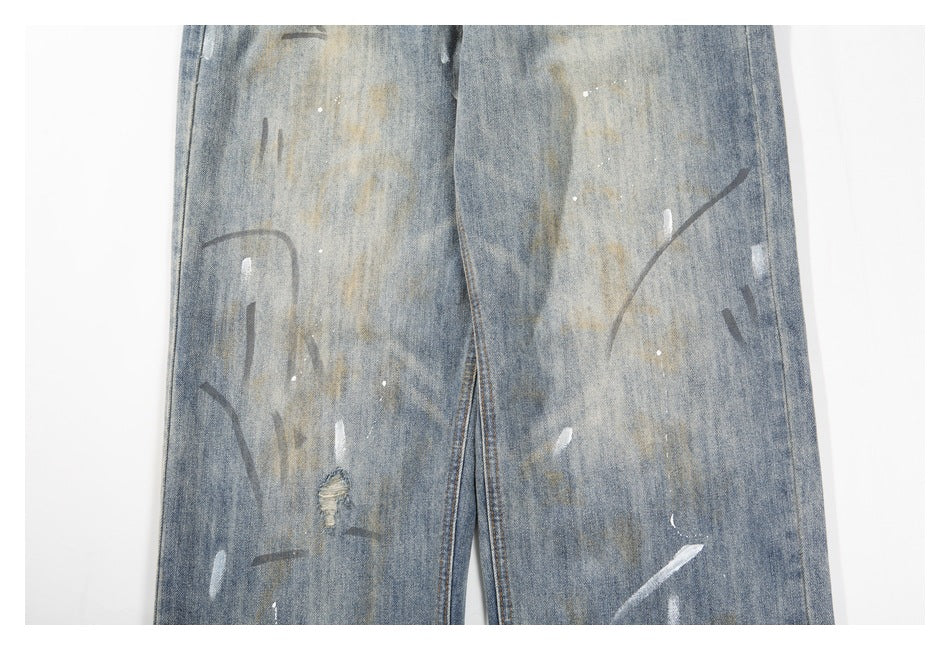 Close-up of the legs of faded blue jeans with paint-like streaks, speckles and a small distressed hole.
