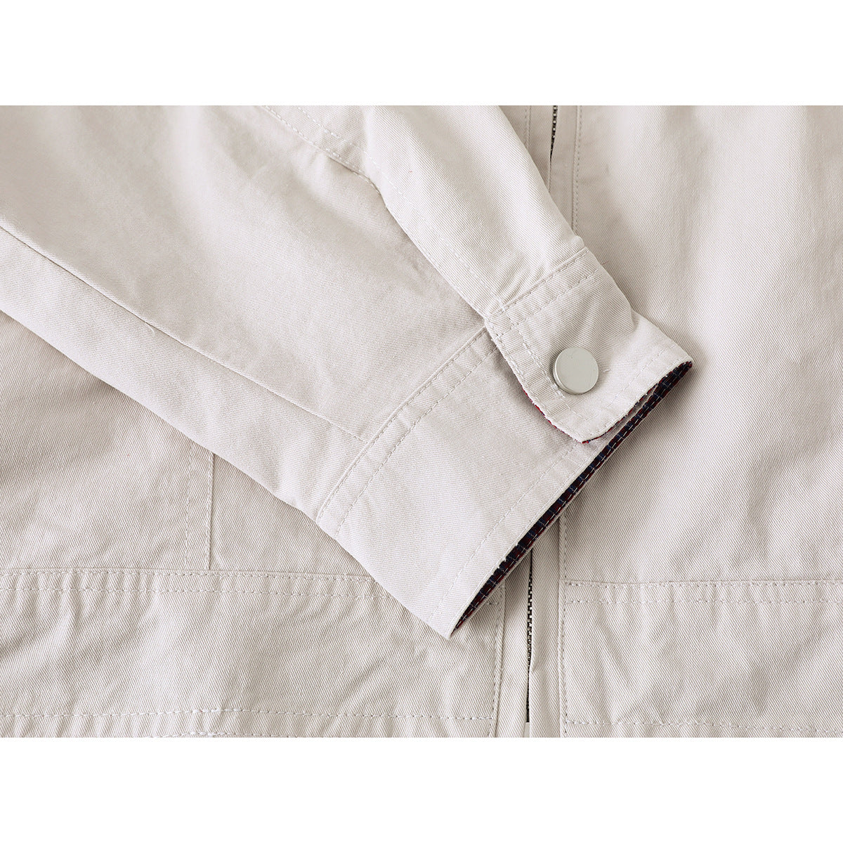 Close-up of an ivory jacket sleeve cuff with a snap button and visible plaid lining.