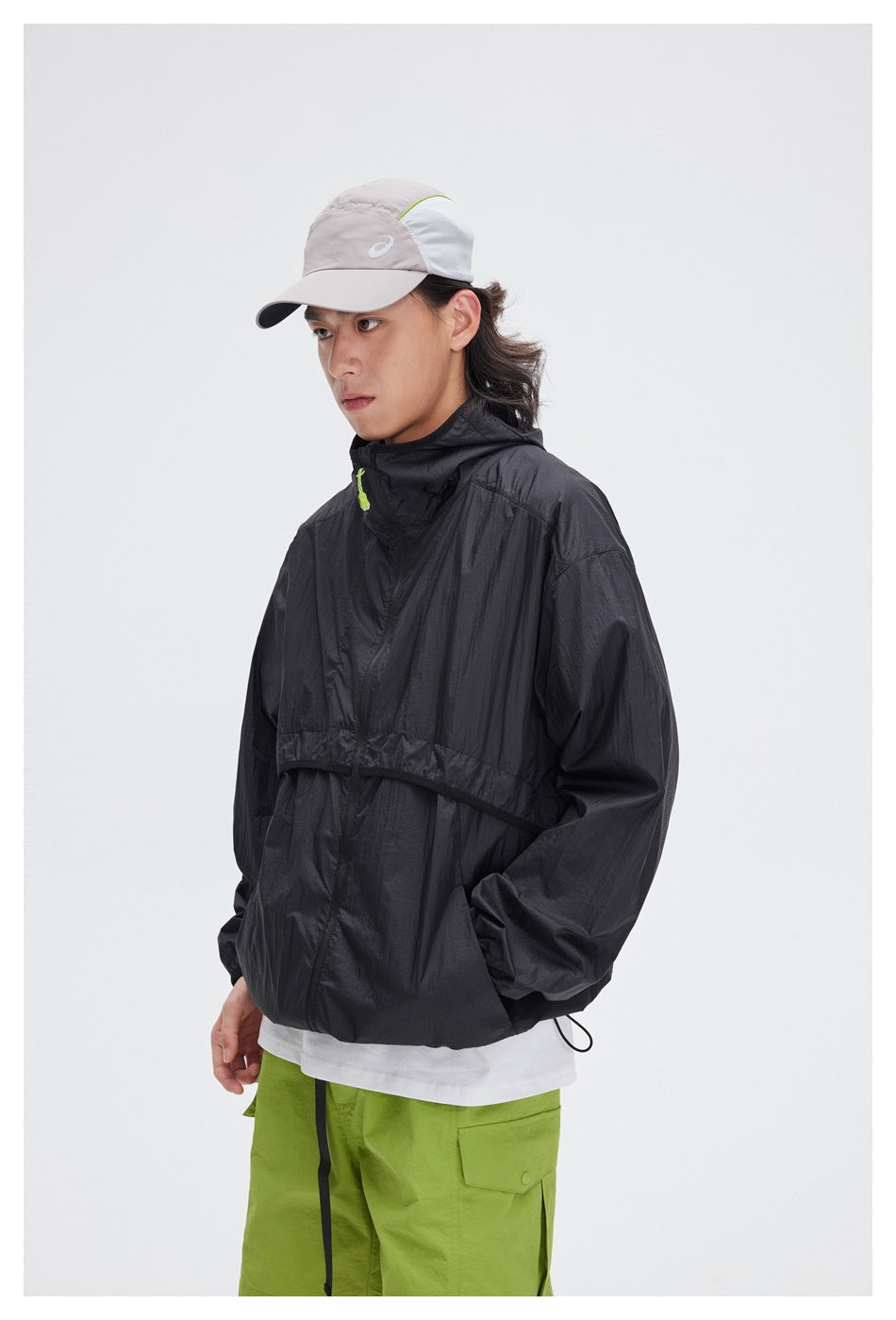 Closer front view of a model wearing a black hooded pullover jacket with lime-green shorts.