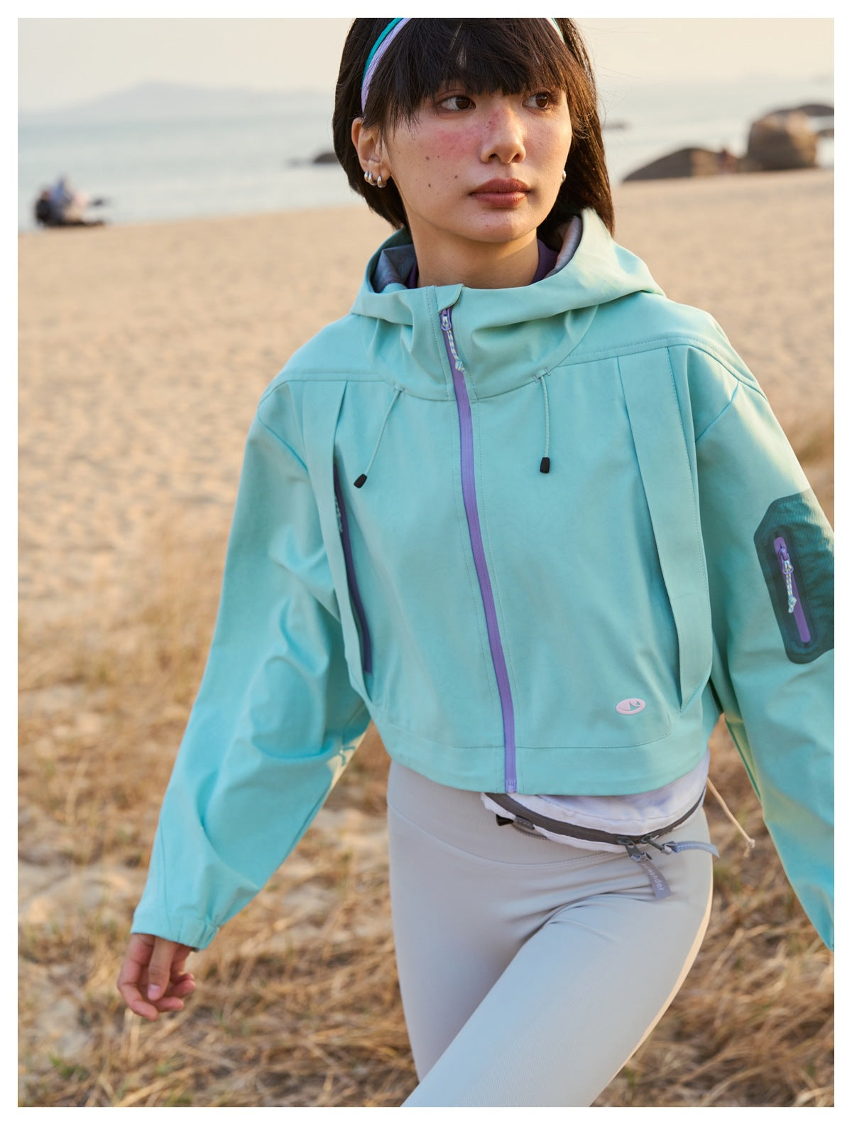 Close view of a model wearing a mint hooded jacket with a purple front zipper and sleeve pocket.