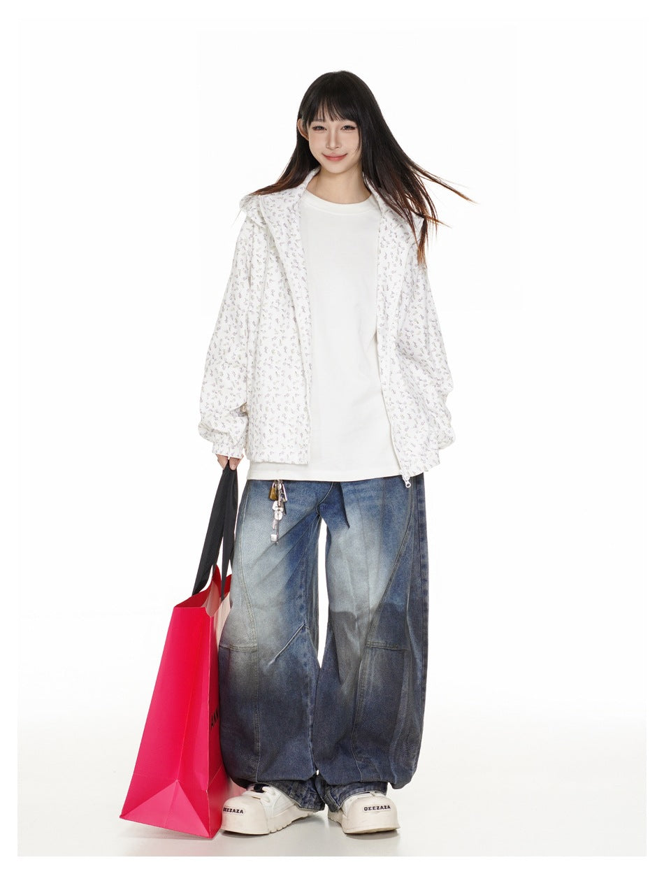 Model wearing white floral hooded jacket open over a white tee with wide-leg faded jeans, holding a pink shopping bag